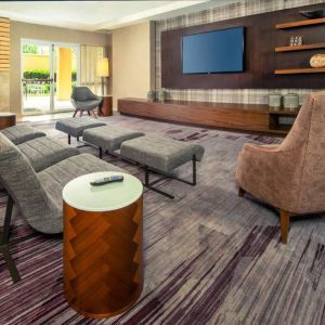 The hotel lobby is furnished with a very large TV, comfortable seating with footstools, a fireplace, and coffee tables.