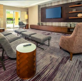 The hotel lobby is furnished with a very large TV, comfortable seating with footstools, a fireplace, and coffee tables.