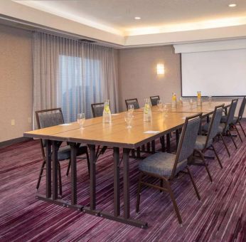 Sonesta Select Allentown Bethlehem Airport meeting room, including long wooden table, projector screen, seating for eight, and window.