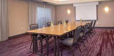 Sonesta Select Allentown Bethlehem Airport meeting room, including long wooden table, projector screen, seating for eight, and window.