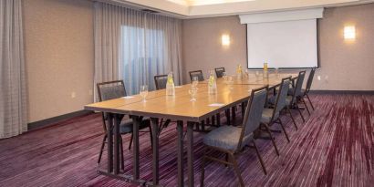 Sonesta Select Allentown Bethlehem Airport meeting room, including long wooden table, projector screen, seating for eight, and window.