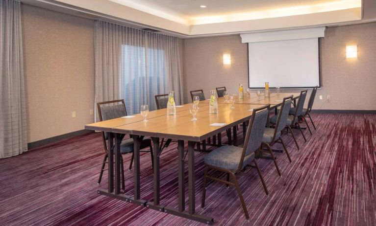 Sonesta Select Allentown Bethlehem Airport meeting room, including long wooden table, projector screen, seating for eight, and window.