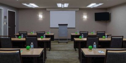 Hotel meeting room, with tables arranged in a classroom format, facing a lectern, TV, and whiteboard.