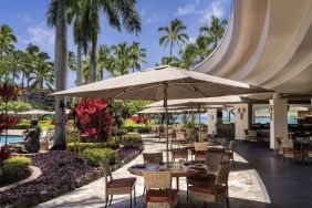 The hotel’s terrace includes dining under shaded cover, with the pool and towering trees nearby.