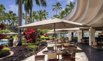 The hotel’s terrace includes dining under shaded cover, with the pool and towering trees nearby.