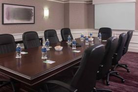 Sonesta Select Boston Lowell Chelmsford meeting room, including long wooden table, nine leather swivel chairs, and a projector screen.