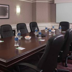 Sonesta Select Boston Lowell Chelmsford meeting room, including long wooden table, nine leather swivel chairs, and a projector screen.