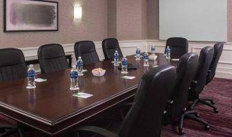 Sonesta Select Boston Lowell Chelmsford meeting room, including long wooden table, nine leather swivel chairs, and a projector screen.