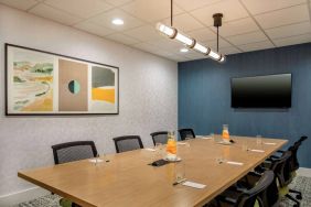 Meeting room in Sonesta Select Boston Foxborough Mansfield with long wooden table, eight chairs, and a large, wall-mounted TV.