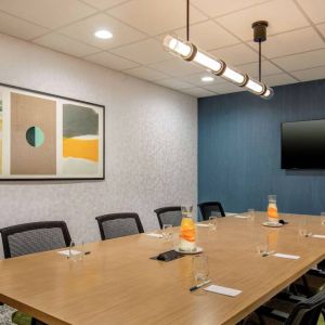 Meeting room in Sonesta Select Boston Foxborough Mansfield with long wooden table, eight chairs, and a large, wall-mounted TV.