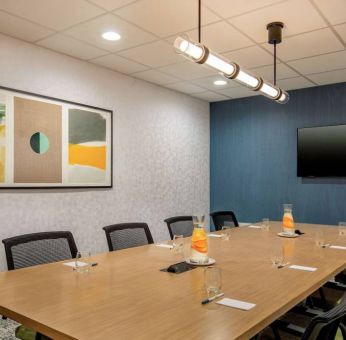 Meeting room in Sonesta Select Boston Foxborough Mansfield with long wooden table, eight chairs, and a large, wall-mounted TV.