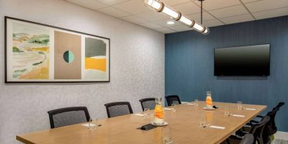 Meeting room in Sonesta Select Boston Foxborough Mansfield with long wooden table, eight chairs, and a large, wall-mounted TV.