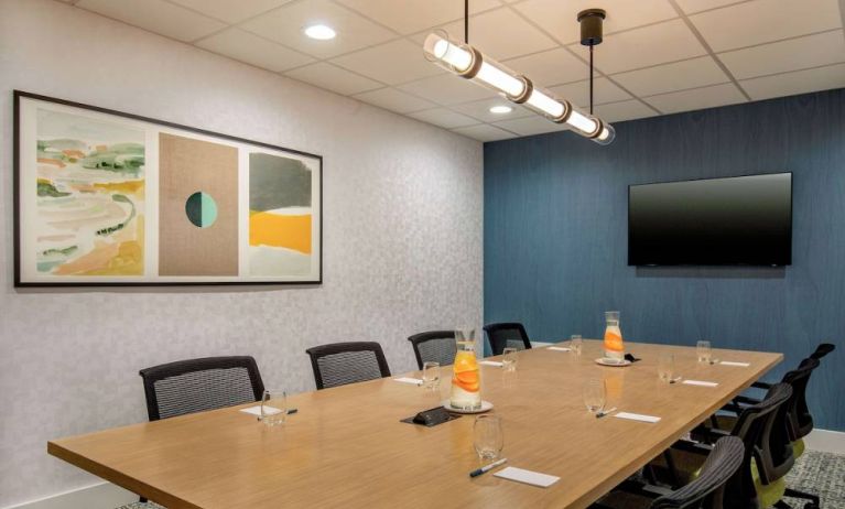 Meeting room in Sonesta Select Boston Foxborough Mansfield with long wooden table, eight chairs, and a large, wall-mounted TV.