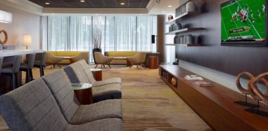 Sonesta Select Atlanta Cumberland Galleria’s lobby has a large, wall-mounted TV, comfortable seating, and coffee tables.