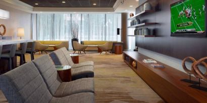 Sonesta Select Atlanta Cumberland Galleria’s lobby has a large, wall-mounted TV, comfortable seating, and coffee tables.