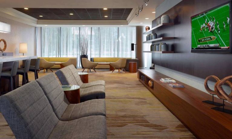 Sonesta Select Atlanta Cumberland Galleria’s lobby has a large, wall-mounted TV, comfortable seating, and coffee tables.