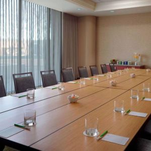 Hotel meeting room, with long wooden table, seating for over a dozen attendees, and large windows.