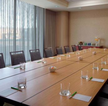 Hotel meeting room, with long wooden table, seating for over a dozen attendees, and large windows.