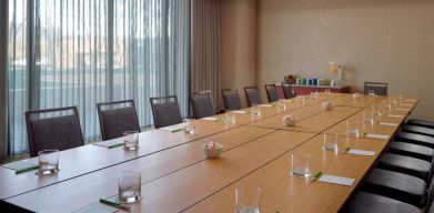 Hotel meeting room, with long wooden table, seating for over a dozen attendees, and large windows.