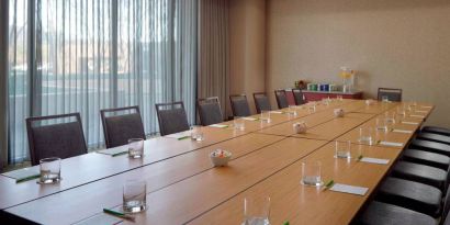 Hotel meeting room, with long wooden table, seating for over a dozen attendees, and large windows.