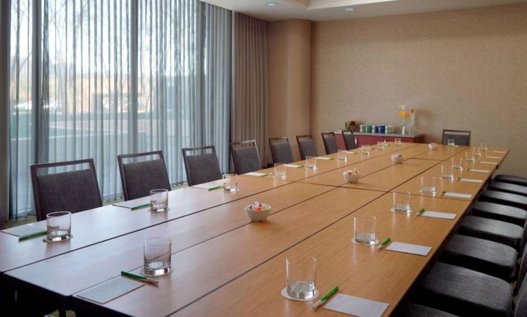 Hotel meeting room, with long wooden table, seating for over a dozen attendees, and large windows.