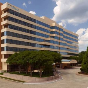 Sonesta Select Atlanta Cumberland Galleria’s exterior has the name on the building, numerous trees, and a covered entranceway.