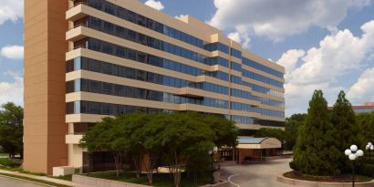 Sonesta Select Atlanta Cumberland Galleria’s exterior has the name on the building, numerous trees, and a covered entranceway.