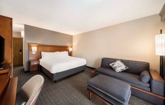 Double bed guest room in Sonesta Select San Jose Airport, furnished with sofa, chair, and TV.