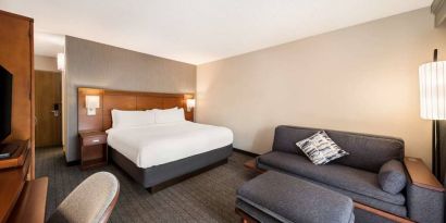 Double bed guest room in Sonesta Select San Jose Airport, furnished with sofa, chair, and TV.