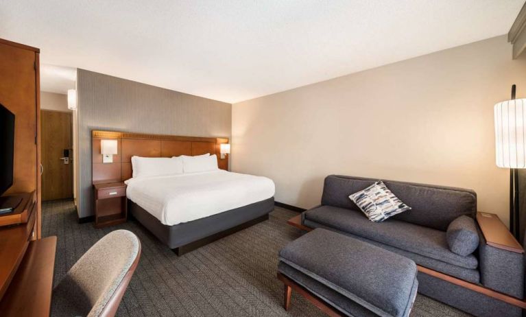 Double bed guest room in Sonesta Select San Jose Airport, furnished with sofa, chair, and TV.