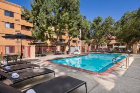 The outdoor pool at Sonesta Select San Jose Airport features a lift, and has nearby sun loungers and shaded tables and chairs.