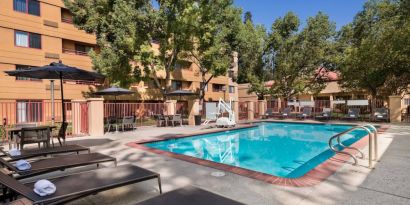 The outdoor pool at Sonesta Select San Jose Airport features a lift, and has nearby sun loungers and shaded tables and chairs.