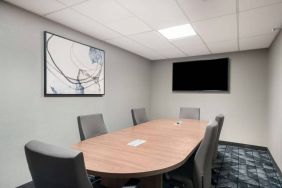 Hotel meeting room, with half a dozen chairs set around a wooden table, and a large TV on the wall.