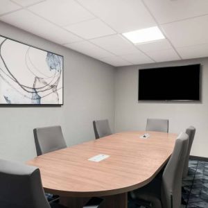 Hotel meeting room, with half a dozen chairs set around a wooden table, and a large TV on the wall.