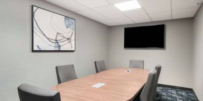 Hotel meeting room, with half a dozen chairs set around a wooden table, and a large TV on the wall.