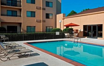 Sonesta Select Charlotte University Research Park’s outdoor pool has sun loungers and a shaded table and chairs by the side.