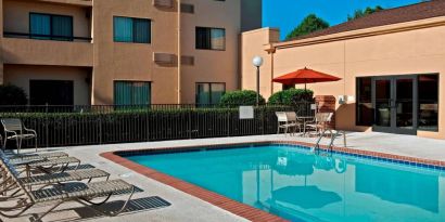 Sonesta Select Charlotte University Research Park’s outdoor pool has sun loungers and a shaded table and chairs by the side.