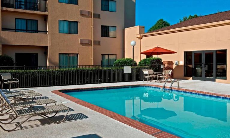 Sonesta Select Charlotte University Research Park’s outdoor pool has sun loungers and a shaded table and chairs by the side.