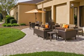 The patio at Sonesta Select Charlotte University Research Park includes sofa and armchair seating, plus coffee tables, near to pleasant greenery.