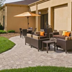 The patio at Sonesta Select Charlotte University Research Park includes sofa and armchair seating, plus coffee tables, near to pleasant greenery.