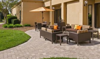 The patio at Sonesta Select Charlotte University Research Park includes sofa and armchair seating, plus coffee tables, near to pleasant greenery.