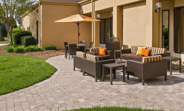 The patio at Sonesta Select Charlotte University Research Park includes sofa and armchair seating, plus coffee tables, near to pleasant greenery.