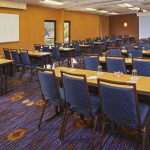 Hotel meeting room, featuring tables arranged in a classroom style facing a projector screen, with a whiteboard to one side.