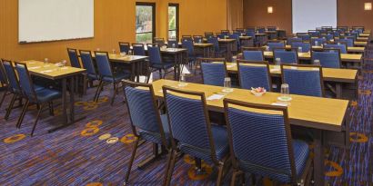 Hotel meeting room, featuring tables arranged in a classroom style facing a projector screen, with a whiteboard to one side.