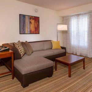 Sonesta ES Suites Charlottesville University guest room living area, including corner sofa, coffee table, TV, and window.