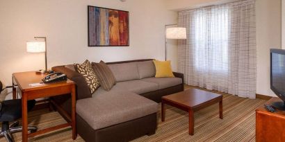 Sonesta ES Suites Charlottesville University guest room living area, including corner sofa, coffee table, TV, and window.