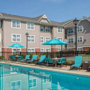 The outdoor pool at Sonesta ES Suites Charlottesville University has a mix of sun loungers and shaded tables and chairs by the side.