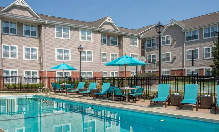 The outdoor pool at Sonesta ES Suites Charlottesville University has a mix of sun loungers and shaded tables and chairs by the side.