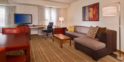 Sonesta ES Suites Charlottesville University guest room workspace, furnished with desk, chair, and TV, plus a sofa.