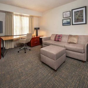 Sonesta ES Suites Baltimore BWI Airport guest room workspace, featuring chair, desk, and TV, plus a sofa nearby.